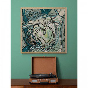 A Simple Heart Framed Print with a record on it next to a green wall.