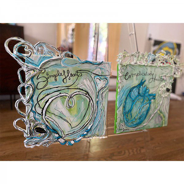Two pieces of Complicated Heart art hanging on a easel.