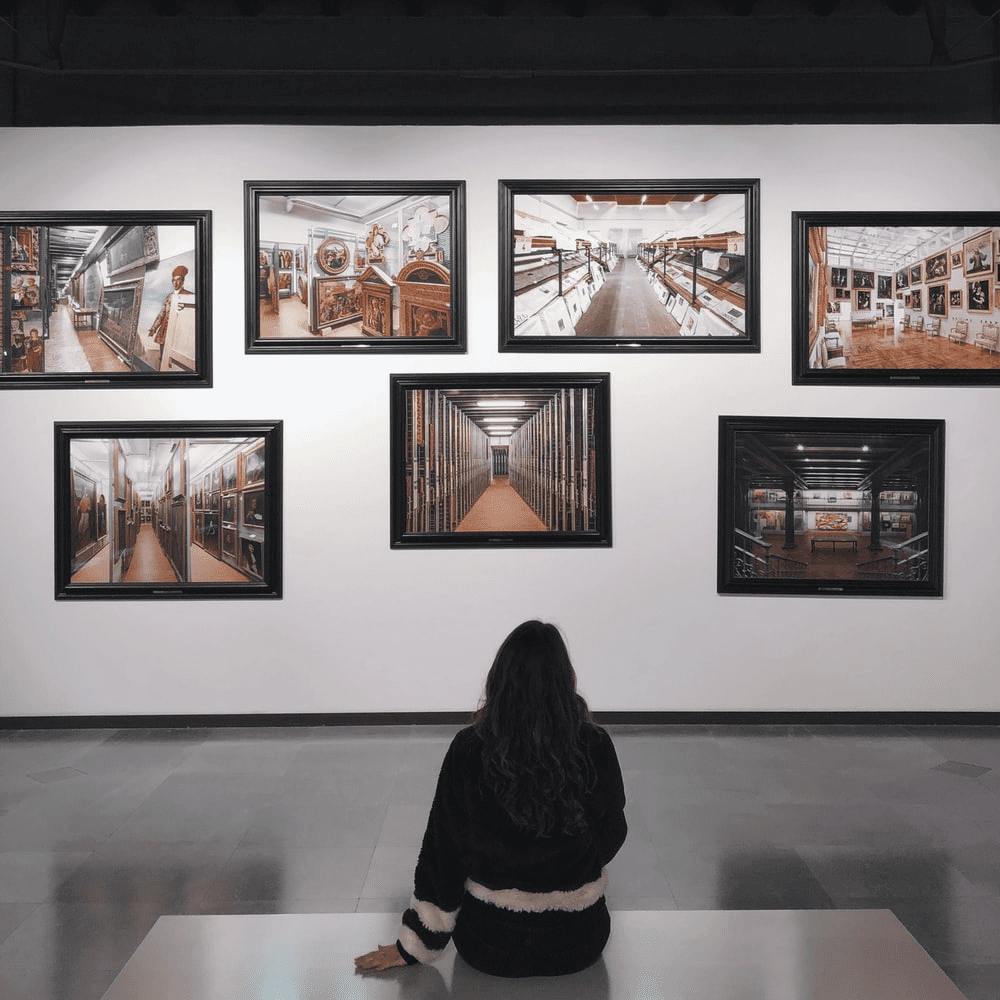 A woman sitting in front of several pictures on the wall.