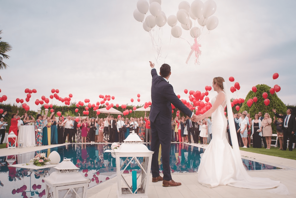 A couple is holding balloons while standing outside.